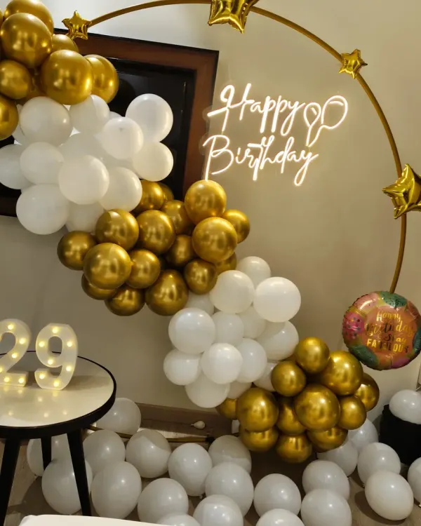 A chic and modern 29th birthday setup. I used a classic gold and white balloon garland on a ring frame, complemented by a custom 'Happy Birthday' neon sign and marquee numbers to create an elegant photo corner.