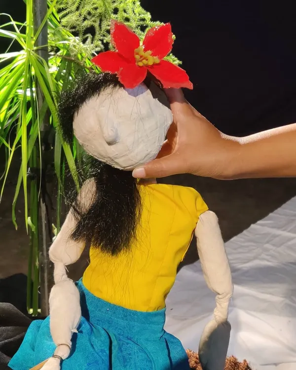 A close-up of a female marionette we built. We use paper mache and simple fabrics to construct the head and body, and a bright red flower gives her a distinct character.
