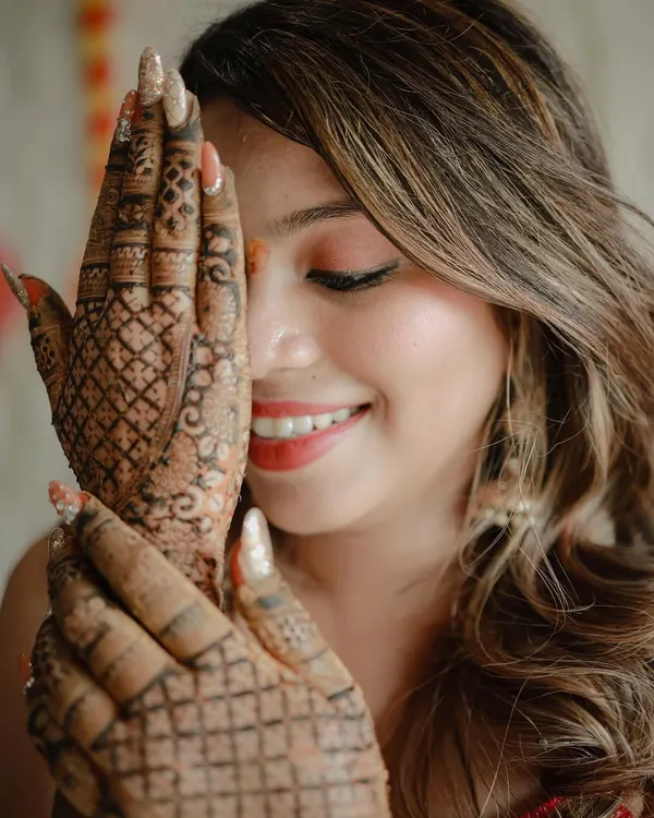A close-up portrait focusing on the bride's beautiful smile and her intricate mehndi design. This shot captures her happiness and the artistry of the henna.