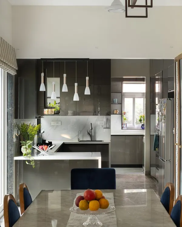 This view shows how the open kitchen seamlessly integrates with the dining area in our Lakshya project. The design prioritizes natural light and an uncluttered feel, with the dining table providing a perfect vantage point to appreciate the sleek, modern kitchen.