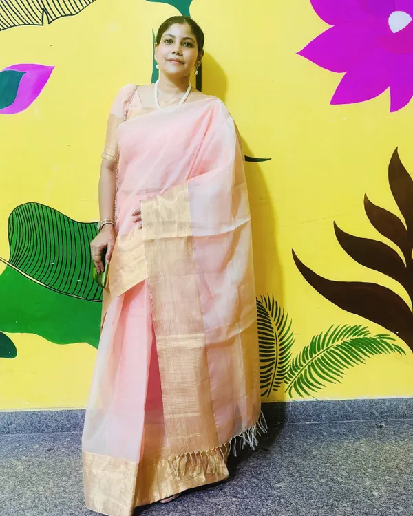 Dressed in a beautiful peach and gold tissue saree for Durga Puja. This full-length shot against a colorful painted wall highlights the elegance of the attire.
