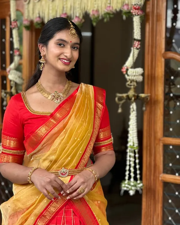 A client glowing in our custom-designed festive half-saree. This classic red and yellow combination is crafted from rich Kanchipuram silk, featuring a traditional checked skirt and a delicate gold border, perfect for any celebration.