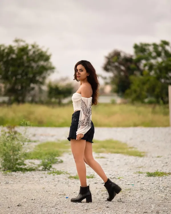 An outdoor portrait set in a field, capturing a candid, windswept moment. The natural setting and casual styling create a feeling of freedom and raw beauty.