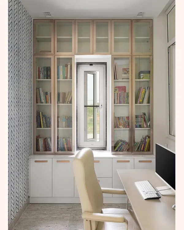 This is the final look of the study nook, built around a window to maximize natural light. The floor-to-ceiling library provides ample book storage, with a mix of glass-fronted and closed cabinets in a two-tone finish.