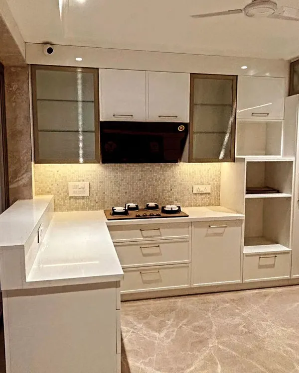 An overview of a beautiful L-shaped kitchen with a breakfast counter. The design combines white cabinets with frosted glass upper units and a textured mosaic backsplash.