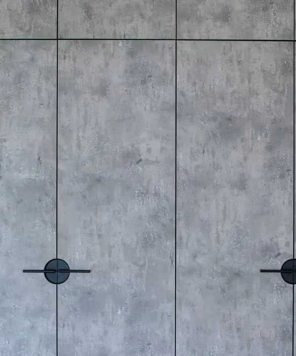 The exterior of the concrete-finish wardrobe. The textured laminate gives it a raw, industrial look that is very modern, while the minimalist black handles add a touch of graphic detail.