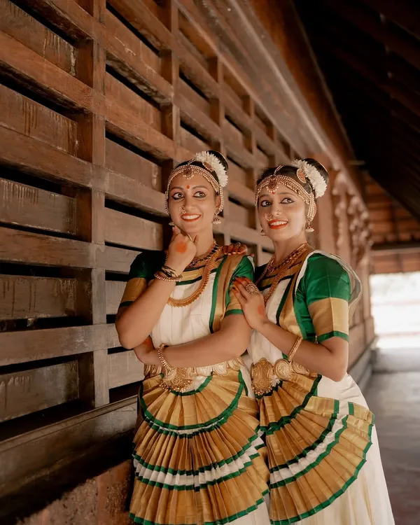 A beautiful portrait of two Mohiniyattam dancers. The composition highlights their synchronized costumes and graceful poses against a traditional architectural background.