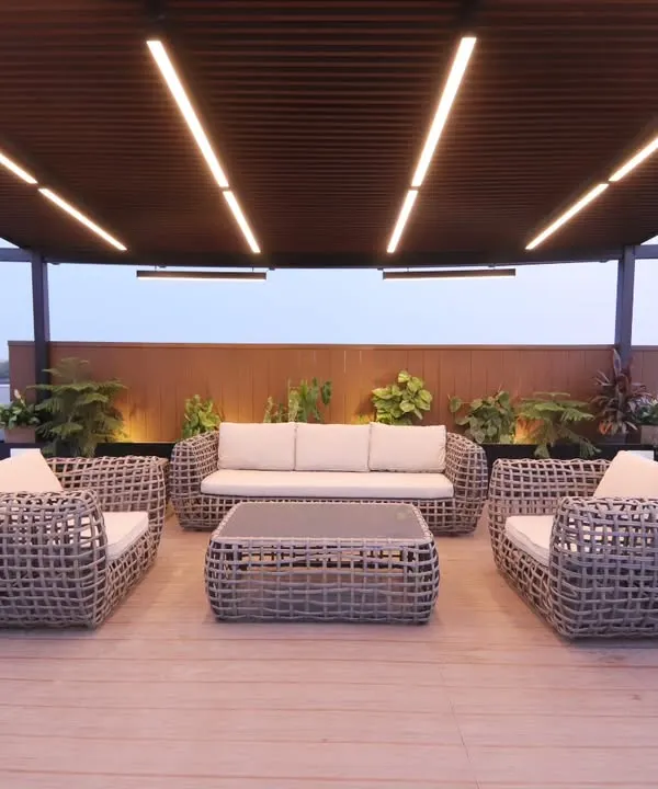 A completed pergola lounge in Palam Vihar, Gurgaon, with modern wicker furniture and integrated ceiling lights. The raised wooden deck clearly defines the seating area.