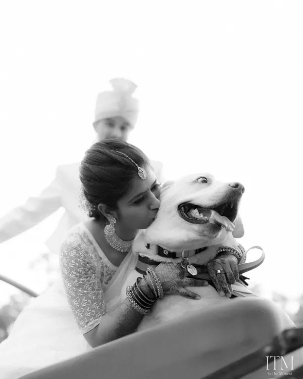 A heartwarming black and white photo of the bride kissing her happy dog. A beautiful, candid moment showing that pets are family too.