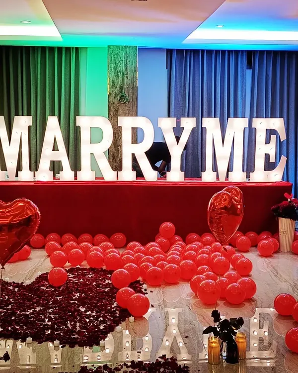 I designed this grand proposal setup in a hotel room, using large marquee letters to create a bold and unforgettable 'MARRY ME' moment. The decor features a classic romantic theme with a dense path of red rose petals, heart-shaped foil balloons, and dramatic lighting to make the occasion truly special.