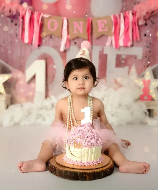 A classic first birthday cake smash portrait. This little girl is ready to celebrate with her pink rosette cake, wearing a party hat and pearls.