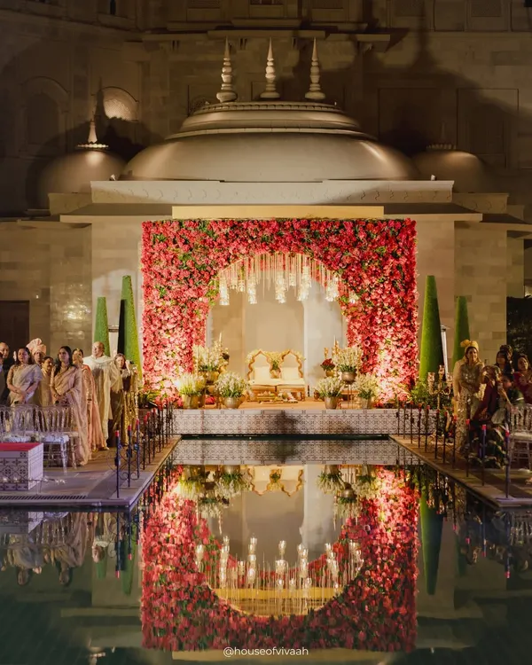 A mandap that appears to float on water. For this wedding at Fairmont Jaipur, we created a breathtaking floral arch reflected perfectly in the still water, surrounded by candles to create a surreal, romantic atmosphere for the ceremony.