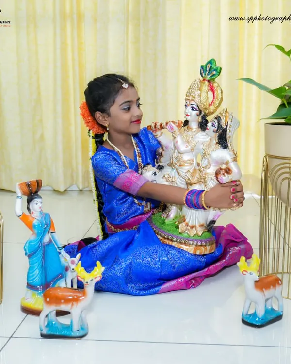A young girl poses with a Krishna statue during a festive studio shoot. We provide props and backdrops to create an authentic and celebratory atmosphere for these special portraits.