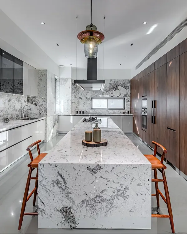 This kitchen, designed for a home in Ahmedabad, is the heart of the house. It features a stunning Brazilian granite island that serves as both a workspace and a gathering spot, complemented by high-gloss lacquer and warm walnut laminate cabinets. The integrated Siemens appliances and Falmec chimney complete this blend of high performance and timeless elegance.
