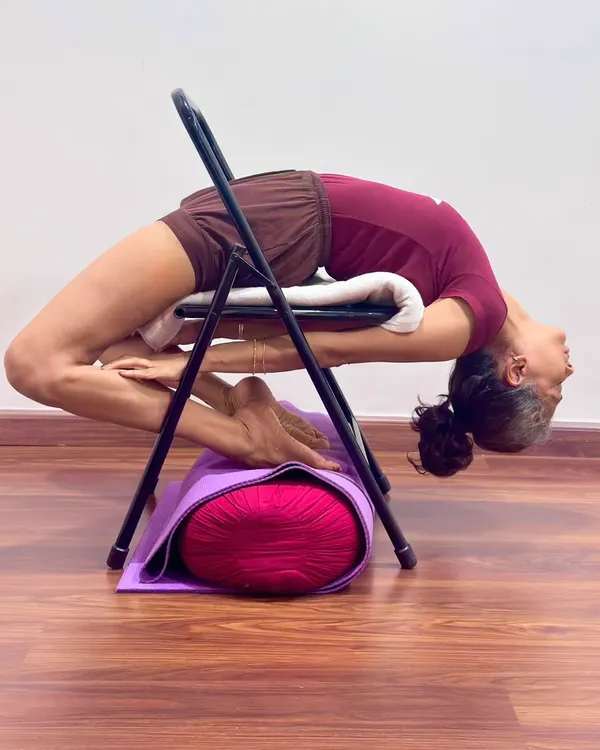 Here, a chair and bolster are used to support the spine in a deep backbend. This setup allows for a safe and extended opening of the thoracic spine and heart center, making the pose both therapeutic and accessible.