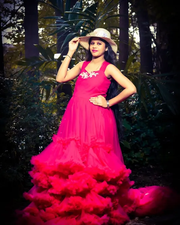 A striking solo portrait in a vibrant pink gown. The hat adds a touch of style, and the dark, moody lighting of the forest backdrop makes the subject and dress pop.