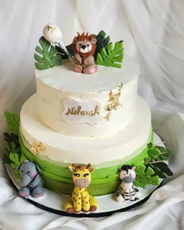 A fun and friendly jungle theme cake. This two-tier cake is filled with gems, kisses, and jellies for a surprise inside. It's decorated with cute, handcrafted fondant animals like a lion, giraffe, and elephant.