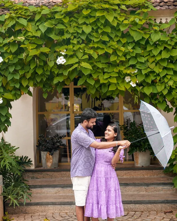 A sweet, playful moment during a pre-wedding shoot in Pondicherry, using a simple umbrella prop against a lush, green backdrop.