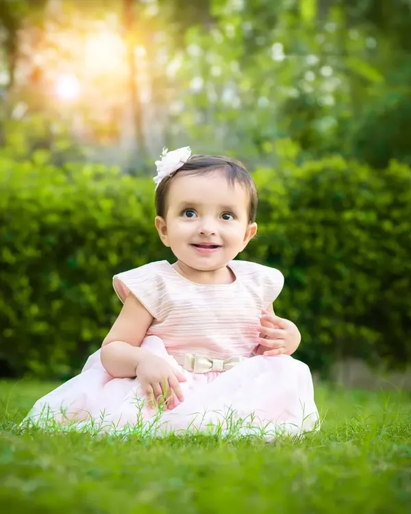 A baby girl sits in a lush green park, the sunlight creating a beautiful halo effect around her. A perfect example of a magical outdoor portrait.