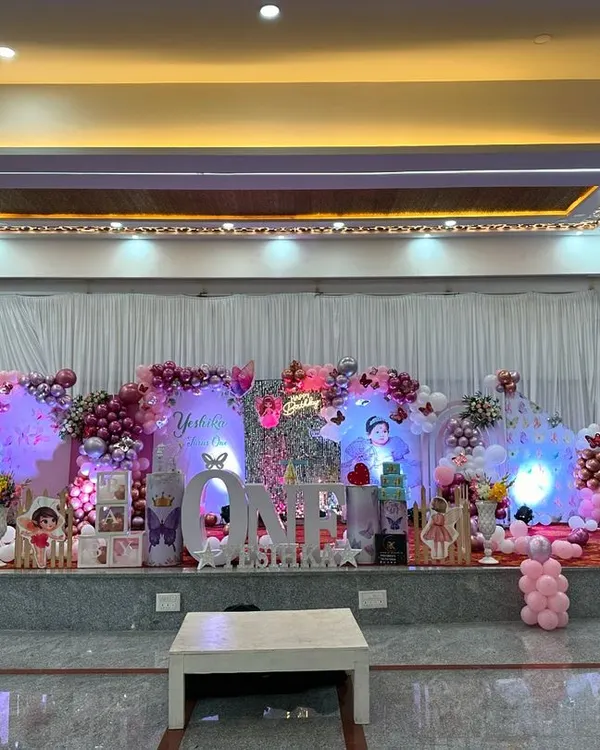 This full-stage butterfly theme is a great example of how I can transform a large banquet hall into a magical wonderland. The setup includes large butterfly wing cutouts, a custom 'ONE' marquee sign, and an elaborate balloon arrangement in pink and purple for a truly grand first birthday celebration.