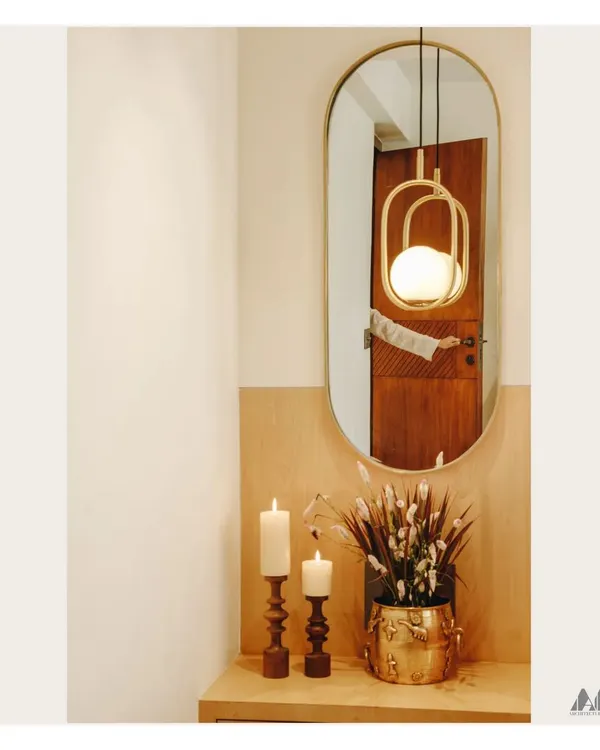 A simple yet elegant corner vignette. The composition of a modern pendant light, an oval mirror, and classic candle holders creates a warm and welcoming ambiance.