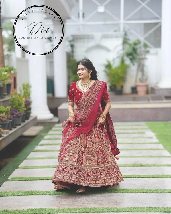 A full-length view of a bride in a magnificent red lehenga. The makeup is classic and elegant, designed to complement the grandeur of her outfit. This is a timeless North Indian bridal look, perfect for making a grand entrance.