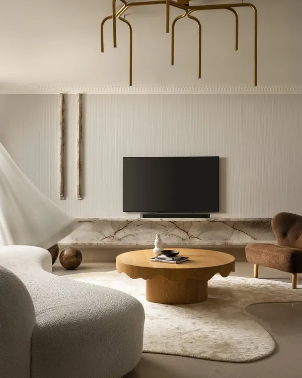A glimpse into the living area of Ecru House, where a fluted wall texture, an organically shaped rug, and a sculptural brass chandelier come together. This composition highlights our focus on warm minimalism and creating visual rhythm through texture and form.