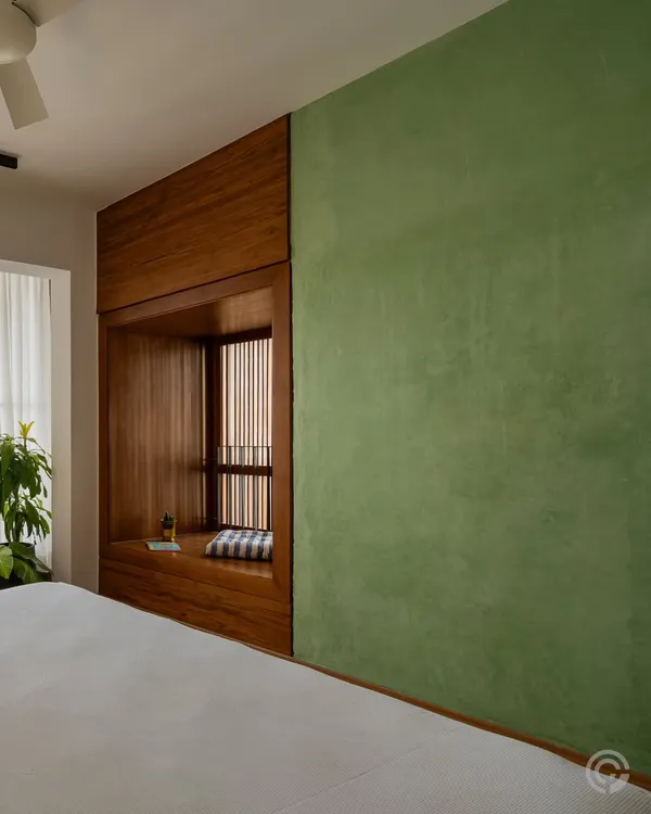 A cozy window seat, framed entirely in wood, is integrated into the bedroom wall. This 'bay window' nook offers a private space for reading and reflection, connecting the room with the outdoors through a slatted screen.