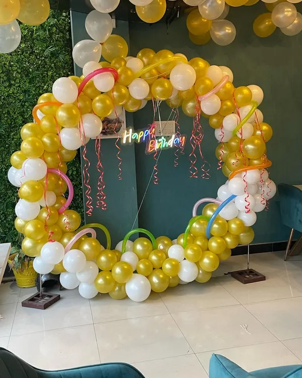 This beautiful balloon ring in gold and white is perfect for birthdays or anniversaries. The setup is enhanced by a custom 'Happy Birthday' neon sign that adds a colorful glow.