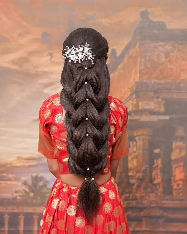 A showcase of an advanced bridal hairdo. This intricate braid is woven with pearls and topped with a beautiful white hair accessory, creating a look that is both traditional and unique.