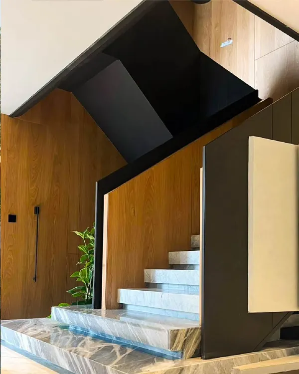 This modern staircase is a statement of minimalist architecture. Crafted from sleek black metal, warm wood paneling, and solid marble steps, the design balances elegance and functionality, creating a sculptural transition between floors.