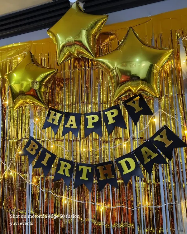 A classic and affordable birthday backdrop. This setup includes a gold foil curtain, a 'Happy Birthday' banner, star-shaped foil balloons, and fairy lights.