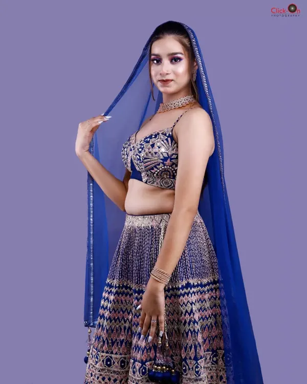 A striking studio portrait against a solid lavender background. The model's royal blue lehenga and sheer dupatta are the focus, demonstrating our skill in capturing traditional wear with a modern, editorial feel.