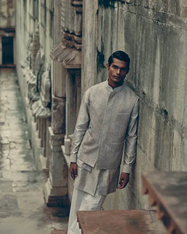A full look from the Dhruv Vaish campaign, shot in a historic stepwell. The layered grey and white ensemble stands out against the ancient stone, creating a look that is both modern and timeless.