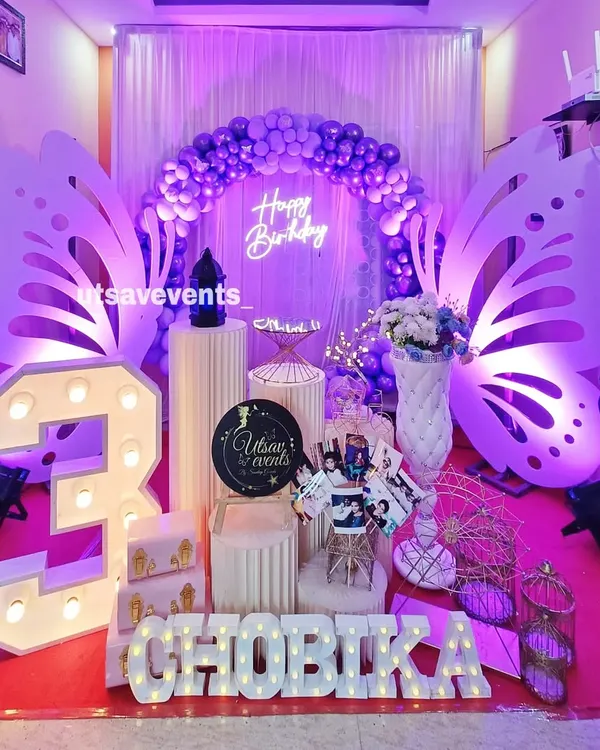 A magical butterfly theme for a third birthday. This setup features large, custom-cut butterfly wings, a soft purple balloon arch, and a glowing neon 'Happy Birthday' sign to create an enchanting photo backdrop.