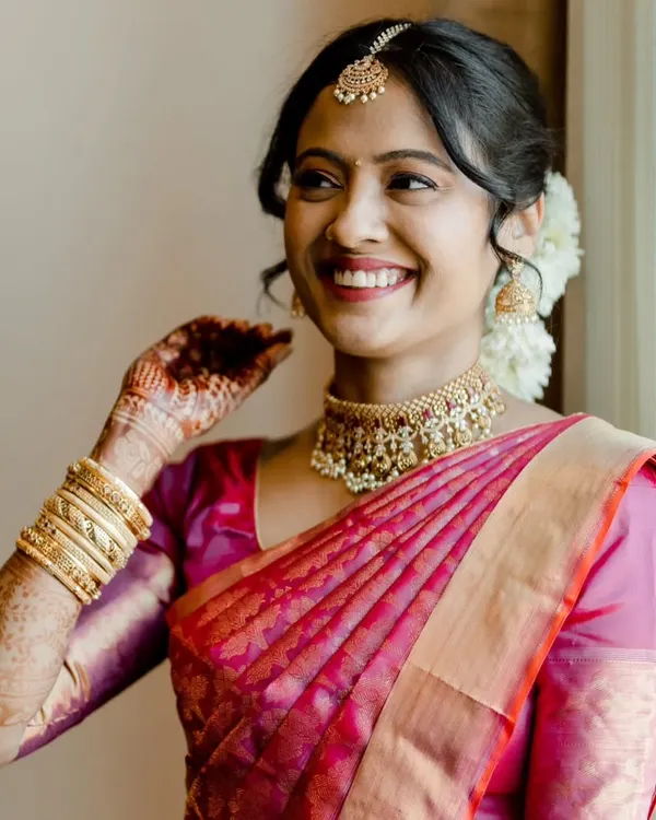 This is what pure joy looks like. For this beautiful South Indian bride, we aimed for a classic look that felt fresh and radiant. The makeup highlights her natural features with a warm, dewy finish, paired with a traditional red lip and a simple bindi. Her hair is styled in an elegant updo, adorned with fresh flowers, completing this timeless bridal look.