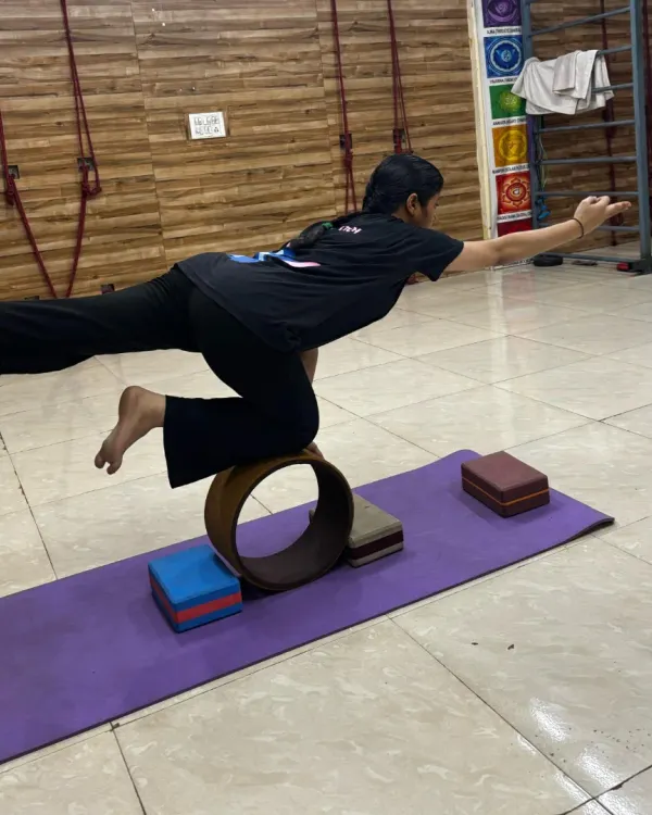A student practices Virabhadrasana III (Warrior III) on a yoga wheel, a powerful pose for building full-body stability.