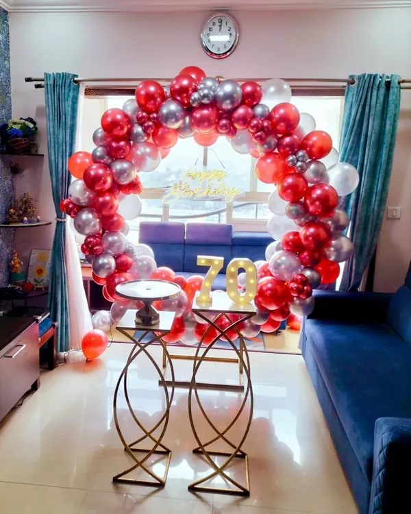 A dazzling 70th birthday home decoration featuring a red and silver balloon ring and large light-up marquee numbers. This setup transforms a living room into a festive party space.