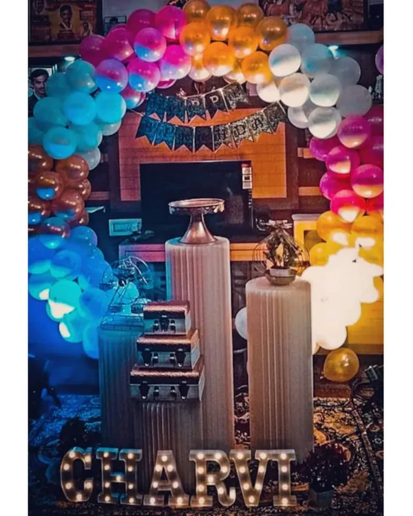 A vibrant and colorful birthday setup featuring a rainbow balloon arch and the name 'CHARVI' in light-up letters. This fun and cheerful decoration is perfect for adding a splash of color to any party.