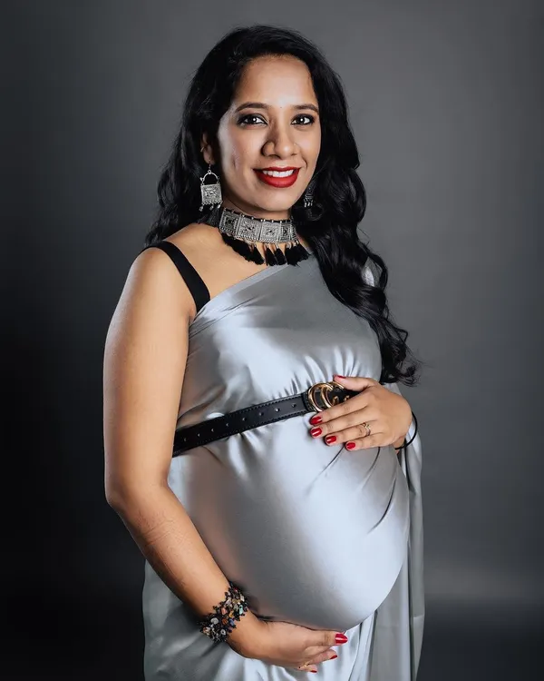 A stunning studio portrait of a mother-to-be, radiating confidence in a modern silver saree styled with a belt. This image showcases a chic and contemporary approach to maternity fashion.