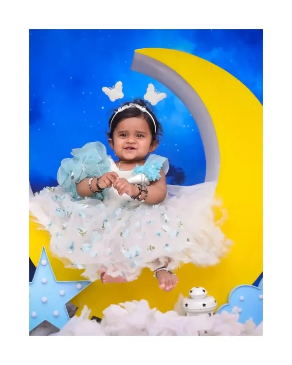 A sweet smile from a 'Moon & Stars' themed session. This little girl is dressed in a beautiful ruffled dress, sitting on a large crescent moon prop against a starry night sky backdrop.
