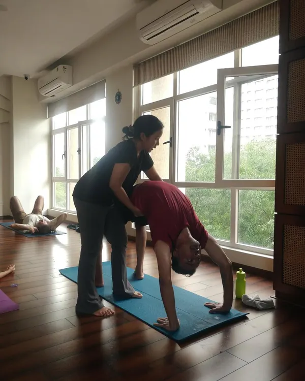 An instructor provides support in Urdhva Dhanurasana, the wheel pose. This hands-on assistance helps the student open the heart and shoulders safely, ensuring the spine is protected while exploring a deeper backbend.