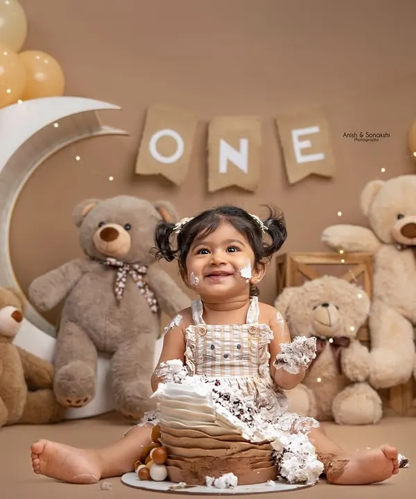This little girl is all smiles during her teddy bear-themed first birthday cake smash. We designed this cozy, neutral-toned setup with a crescent moon, balloons, and lots of cuddly friends for her special milestone.