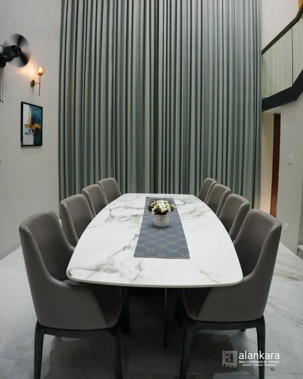 This dining setup is designed for grand entertaining. The large, marble-finish tabletop provides a luxurious surface, surrounded by ten fully upholstered chairs for maximum comfort. The floor-to-ceiling curtains add a touch of drama and sophistication to the double-height space.