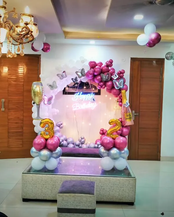 A sophisticated 32nd birthday decoration at home. The setup includes a circular backdrop with pink and silver balloons, butterfly accents, and large number foil balloons, all elegantly arranged around a glass table.