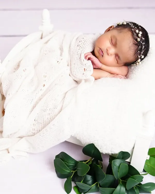 A perfect, peaceful newborn sleeping on a tiny white bed prop, swaddled in a soft white blanket. An angelic and timeless portrait.