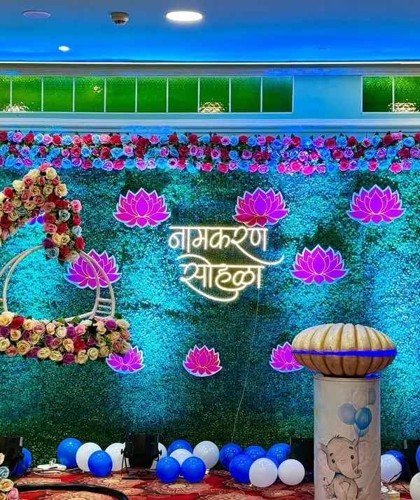 This Namkaran Sohala stage is one of my favorites. I used a lush green wall as the base, adding bright neon lotus flowers and Marathi calligraphy to create a modern yet traditional look. The hanging floral cradle becomes the perfect centerpiece for the baby.