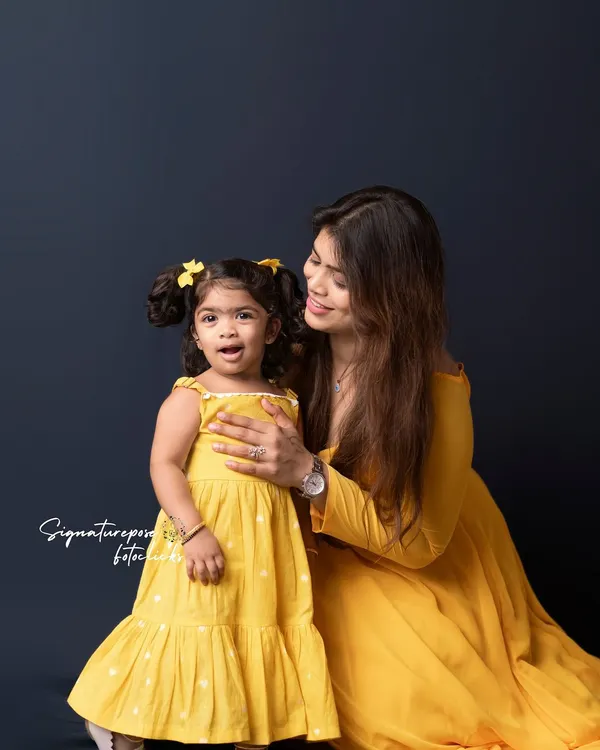 A beautiful moment of connection between a mother and her daughter. Dressed in coordinating yellow outfits, their shared smile is the focus of this simple and elegant studio portrait.