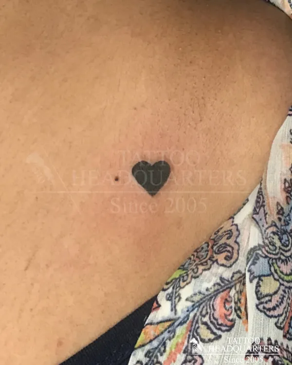 A tiny, solid black heart tattoo on the collarbone. This minimalist design is a perfect example of a simple yet meaningful piece.