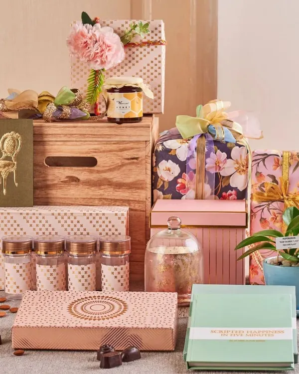 This festive hamper is curated for Diwali, featuring a mix of modern and traditional items. It includes dry fruits, chocolates, a live plant, and beautifully wrapped gift boxes in floral and polka-dot prints.